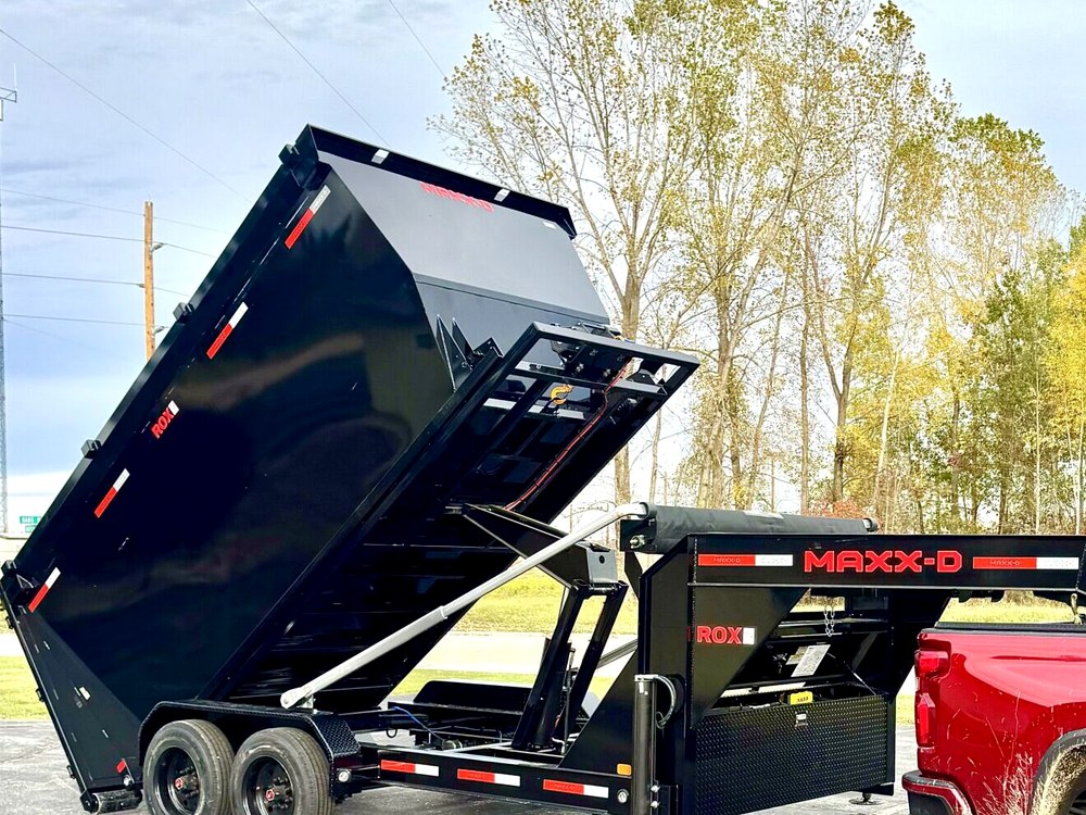The raised body of a black gooseneck dump trailer tipping a load, photographed from the side