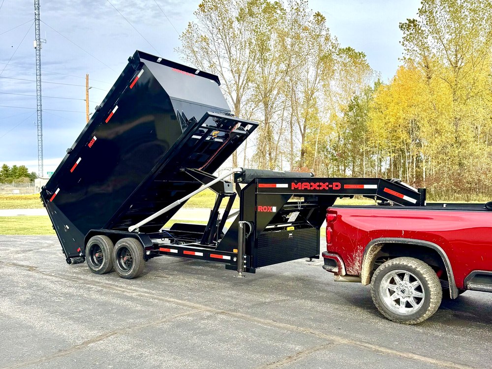 A black gooseneck dump trailer with the body raised, tipping a load onto the ground