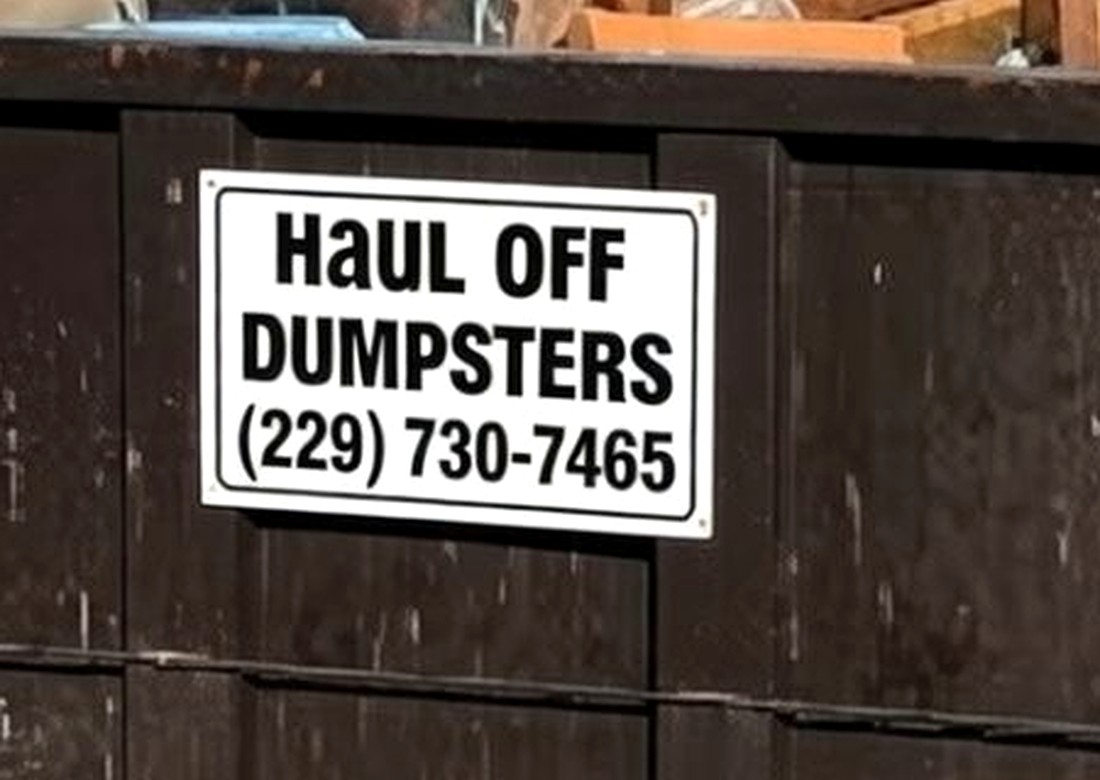 A close view of the white Haul Off Dumpsters sign plate bolted to the side of a roll-off container, showing the business name and phone number